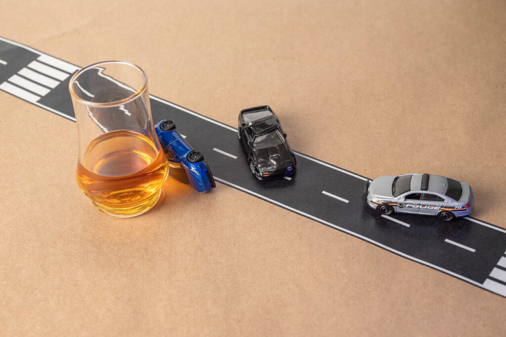 Damaged cars and spilled alcohol at a crash scene, with police lights flashing. This image underscores the potential consequences of drunk driving and the need for legal representation, such as hiring an personal injury attorney, if you've been injured.