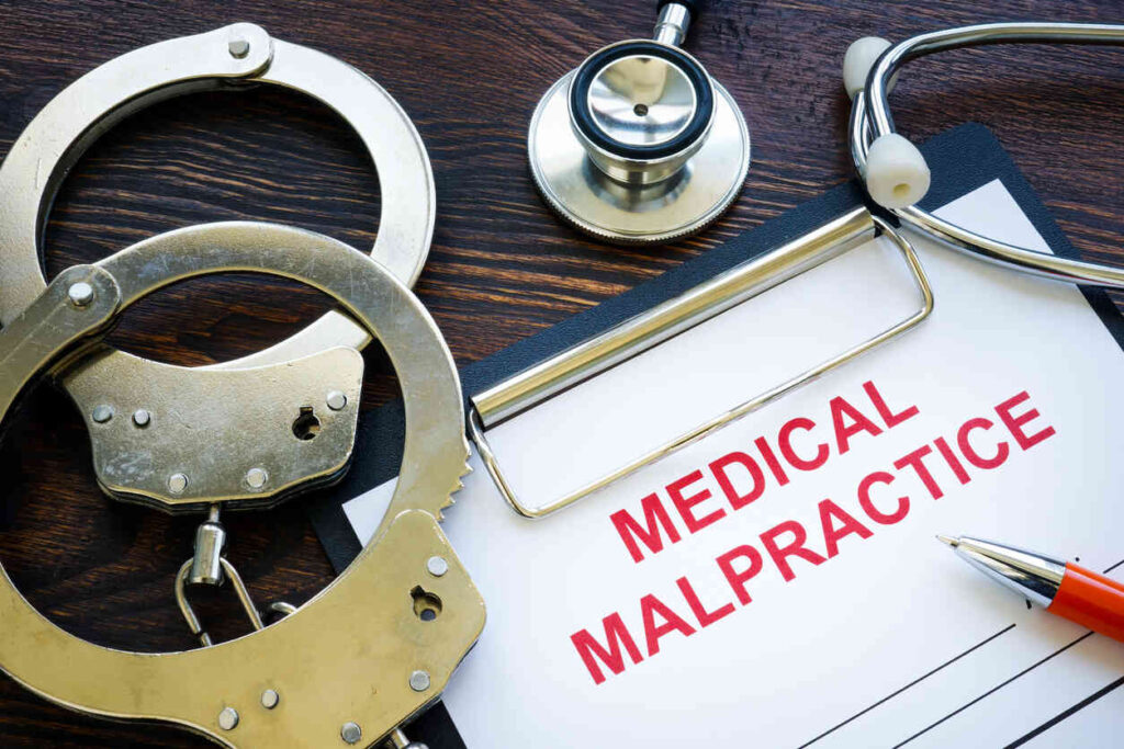 Handcuffs and stethoscope on a clipboard with 'MEDICAL MALPRACTICE' in red letters, symbolizing legal consequences in healthcare