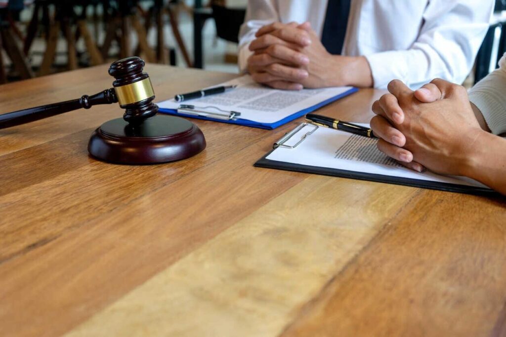 clipboards with legal documents and two individuals with clasped hands, suggesting discussions around a pre-trial settlement in a injury cases