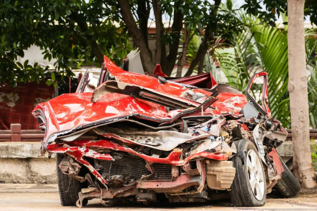A red car severely damaged from an accident, with the front and side crushed, making it appear totaled.